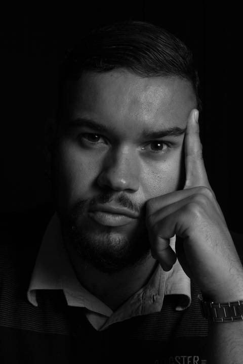 Rafael apoiando a mão sobre o rosto, sério, em estúdio com fundo preto.'