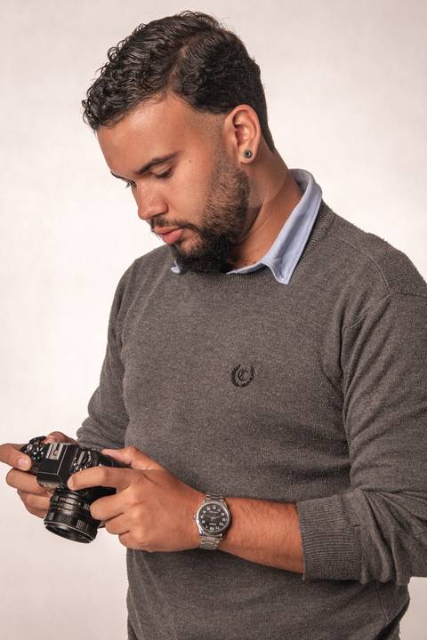 Rafael, em estúdio com fundo branco, segurando uma câmera fotográfica, com o olhar direcionado para o equipamento.'