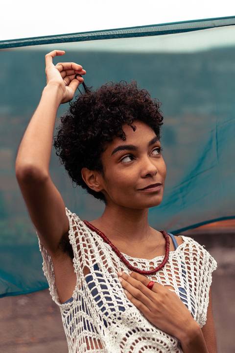 Larissa olhando o horizonte, com a mão em seu cabelo, fundo de tecido azul marinho.'