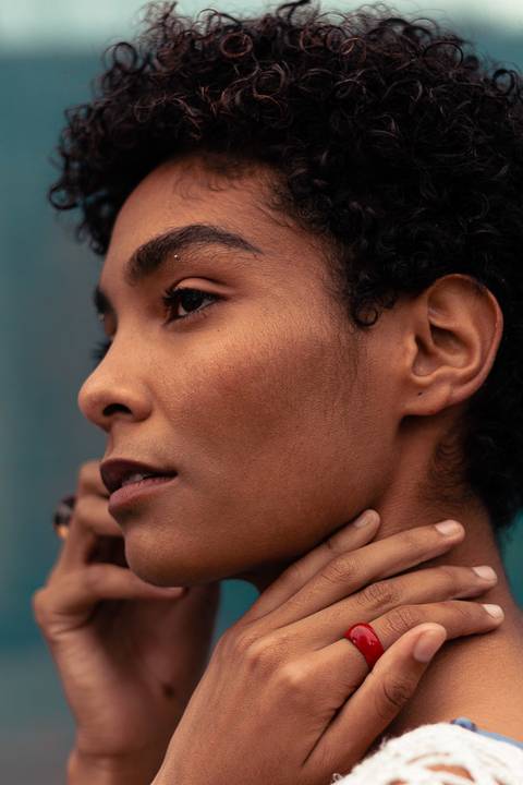Larissa olhando para o horizonte, com as mãos próximas ao rosto, fundo de tecido azul marinho.'