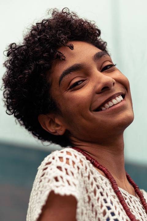 Larissa sorrindo, mostrando suas covinhas, fundo de tecido azul marinho.'