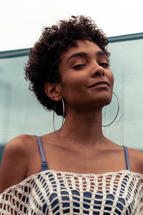Larissa com o olhar direcionado para a câmera, sorrindo leve, fundo de tecido azul marinho.'