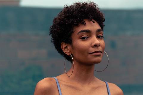 Larissa com o olhar direcionado para a câmera, sorrindo leve, enquadramento frontal, fundo de tecido azul marinho.'