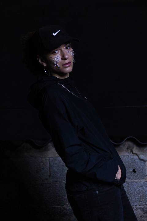 Lariane em cima da laje de uma residência, na zona leste da capital de são paulo. olhando diretamente para mim, repleta de brilhos sob o rosto. rosto bem enquadrado. séria. o corpo inclinado para trás.'