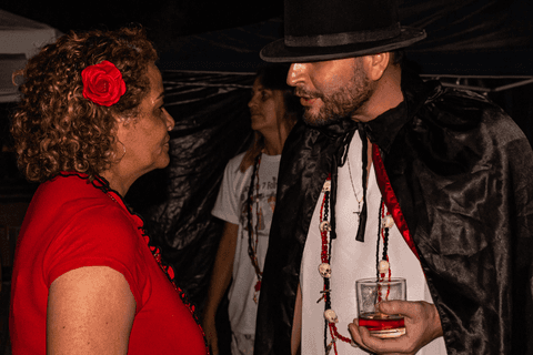 Religiosos incorporados conversando em evento religioso umbandista na praia grande, com flores, guias e copo de bebida em mãos.'