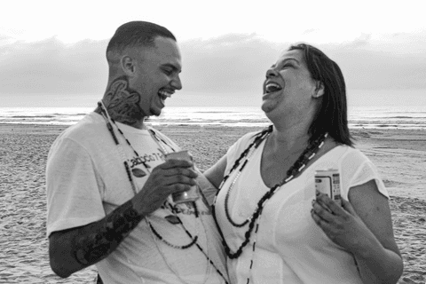 Marinheiros gargalhando em frente ao mar, com latas de cerveja nas mãos.'