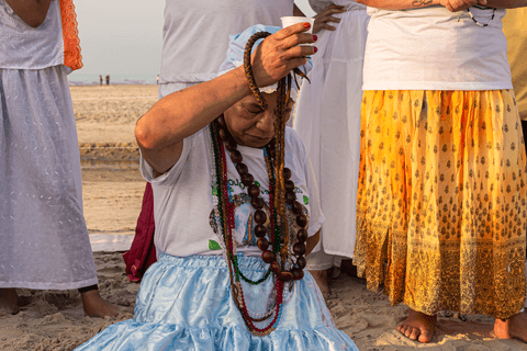 Entidade ajoelhada na areia com suas guias.'