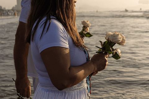 Pessoas segurando rosas brancas dentro do mar, dia amanhecendo.'