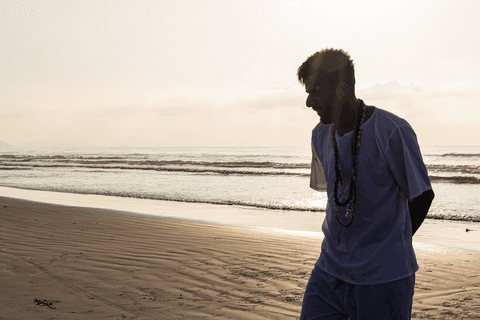 Integrante do terreiro saindo do mar, já pisando na areia, sol ao fundo.'