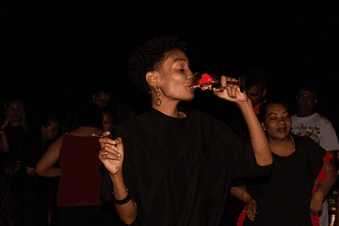 Integrante do terreiro incorporada com pomba-gira, bebendo taça de destilado.'