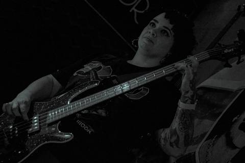 Show da ultra 77 no Armazém 77 aline olhando para a frente, tocando seu baixo, séria'