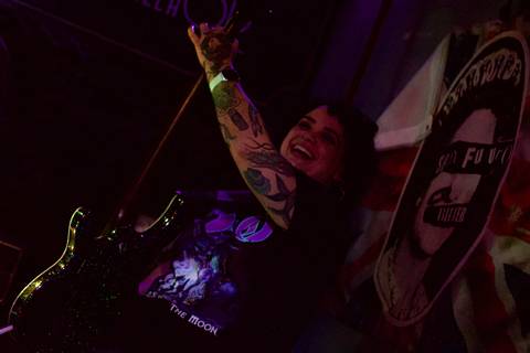 Show da ultra 77 no Armazém 77 aline fazendo movimentos com seu baixo roxo, com sorrido no rosto'