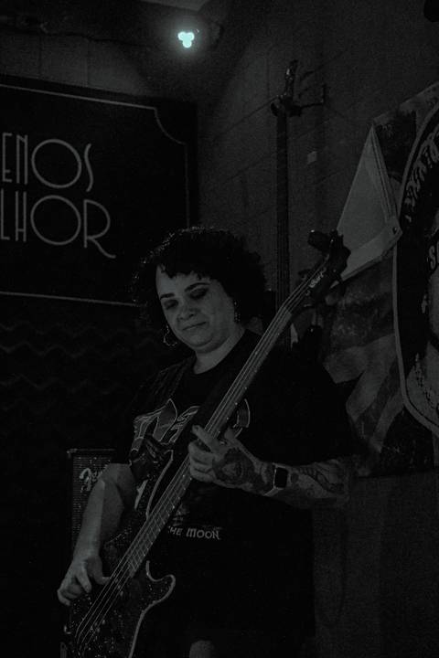 Show da ultra 77 no Armazém 77 aline com seu baixo focada, olhando para ele, foto em preto e branco'