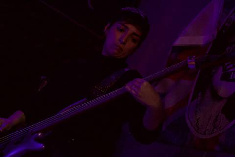 Show da ultra 77 no Armazém 77 lilian tocando seu instrumento, olhando diretamente para ele, com uma iluminação rosa e roxa'