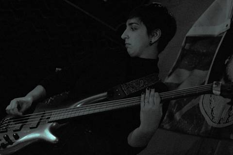 Show da ultra 77 no Armazém 77 lilian olhando para o outro lado, tocando seu baixo, foto em preto e branco, fundo da foto bandeira de cerveja'