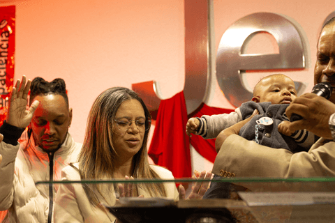 bryan sendo apresentado na igreja, com seus pais em cima do palco ao seu lado'