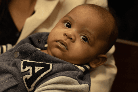 bryan olhando diretamente para a câmera, no colo de sua mãe, dentro da igreja'