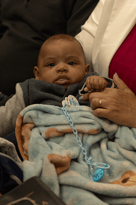 Bryan no colo de sua avó, dentro da igreja, durante sua apresentação perante a todos'