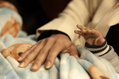 a mão da mãe de bryan sobre seu cobertor, enquanto a mão de bryan está perto'