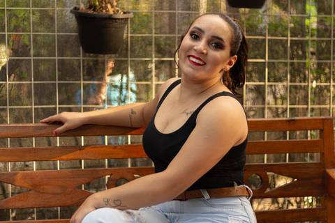 isabel sentada no banco dentro da estufa do parque max feffer olhando para a câmera e sorrindo'