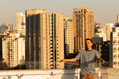 jerf no terraço do mac em pé segurando o corrimão, prédios da cidade ao fundo'