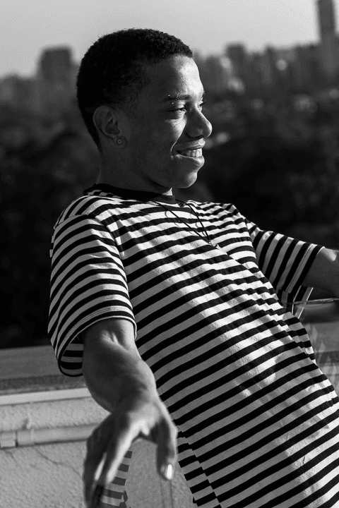 jerf no terraço do mac em pé segurando o corrimão, prédios da cidade ao fundo, sorrindo'