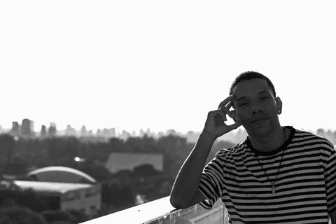 jerf no terraço do mac apoiando o braço no corrimão, olhando diretamente para a câmera'