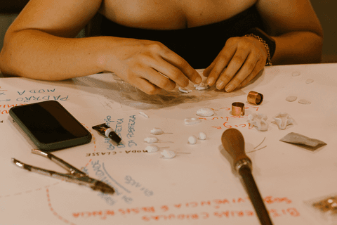 sesc paulista oficina de criação de jóais, parte da mesa em que aluna trabalha, com escritas e muitas pecinhas e ferramentas'