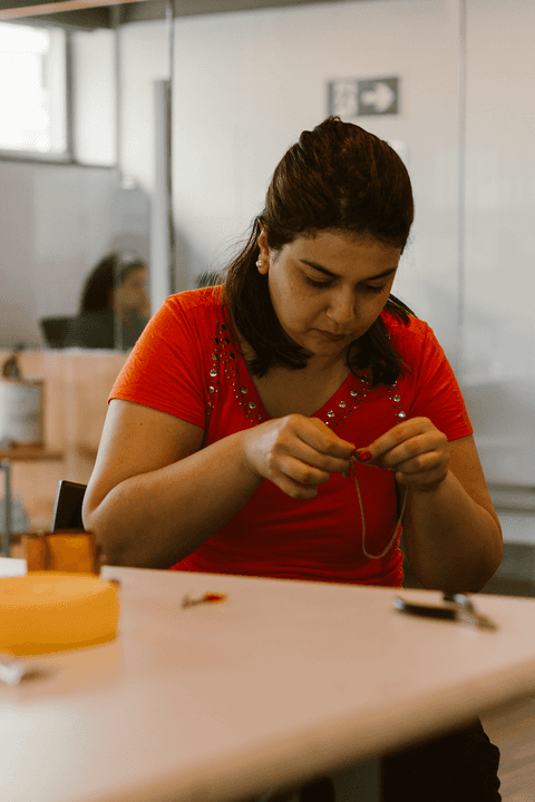 sesc paulista oficina de criação de jóais, aluna arrumando os últimos detalhes das suas jóias, enquanto está sentada na cadeira em frente a mesa'