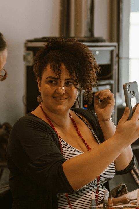 sesc paulista oficina de criação de jóais, aluna com suas peças no rosto, se olhando no celular e mostrando para a professora'