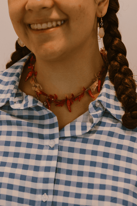 sesc paulista oficina de criação de jóais, outra aluna finaliza suas criações, colar com pimentas e conchas, sorrindo, com suas belas tranças'