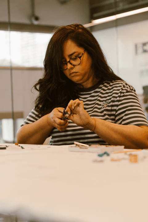 sesc paulista oficina de criação de jóais, aluna de óculos, sentada em frente a mesa de criação'