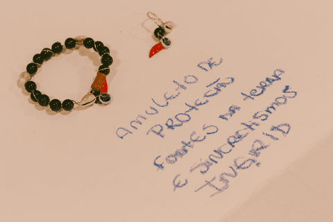 sesc paulista oficina de criação de jóais, pulseira e brinco sobre a mesa, cartolina e frase que remete a essência da aluna e da criação de suas peças'