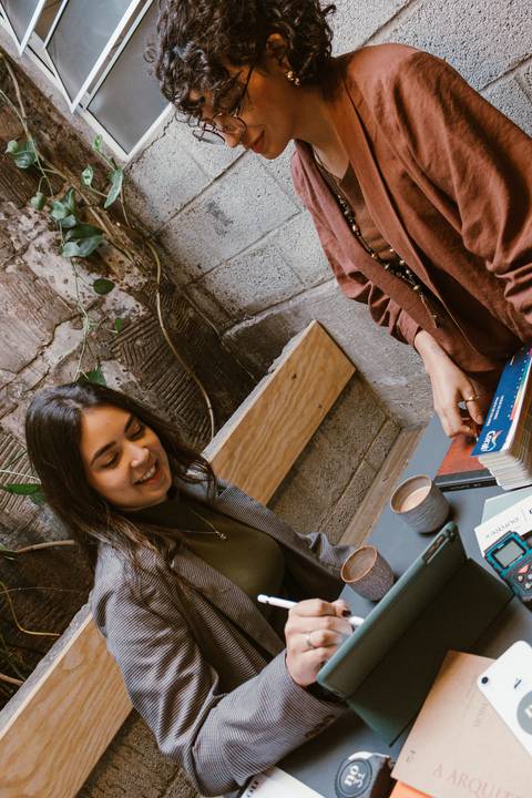 ni sentada em frente a mesa enquanto le conversa com ela encostada na parede'