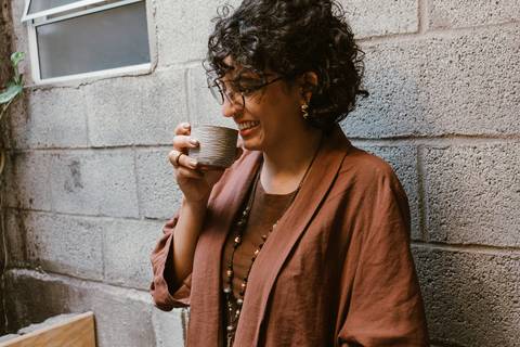 le tomando seu cafezinho encostada na parede em frente a mesa que ni esta sentada trabalhando'