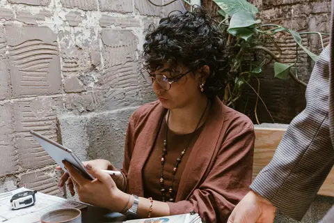 agora le esta sentada enquanto ni esta em pé ao lado da mesa, le com o tablet'