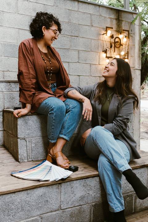 le e ni sentadas na escadaria da cafeteria ao lado de fora, enquanto se olham e sorriem'