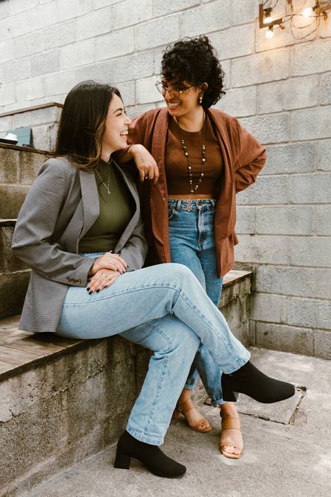 le e ni na escadaria da cafeteria ao lado de fora, ni sentada enquanto le em pé apoia o braço em ni se olhando, sorrindo felizes'