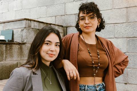 le e ni na escadaria da cafeteria ao lado de fora, ni sentada enquanto le em pé apoia o braço em ni olhando serias para a câmera'
