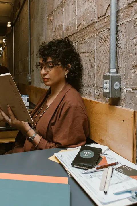 leticia sentada a mesa da cafeteria lendo um livro de arquitetura'