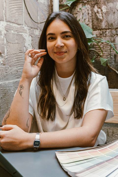 nicole com o braço apoiado na mesa, olhando para mim, ssorriso leve, com a mão sobre o rosto'