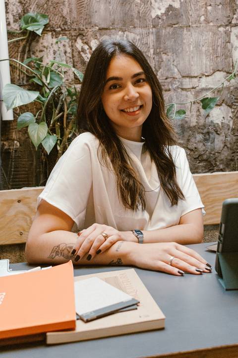 nicole sentada com os braços entrelaçados sobre a mesa, sorrindo com seu tablet a frente dela'