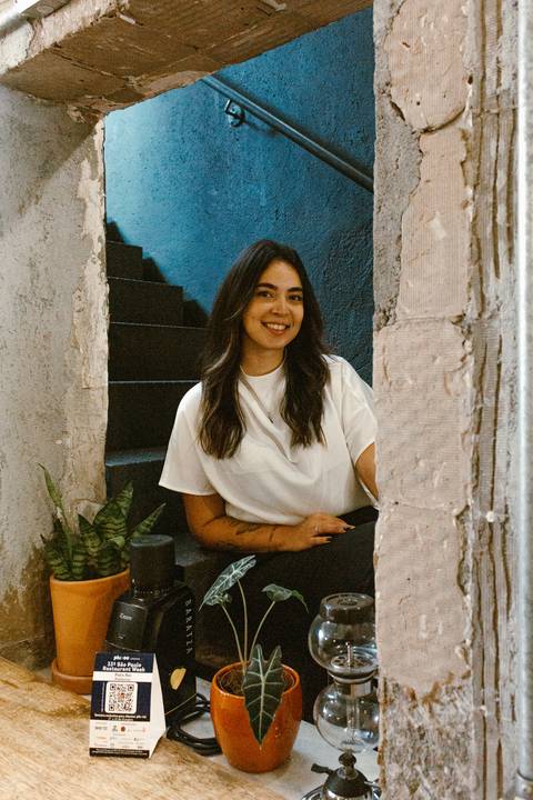nicole sentada na escadaria na parte de dentro da cafeteria, olhando para amim enquanto sorri'
