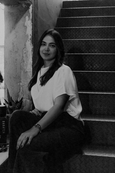 nicole sentada na escadaria na parte de dentro da cafeteria, olhando para a frente em foto preto e branco, novo ângulo'