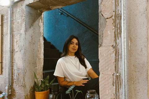 nicole sentada na escadaria na parte de dentro da cafeteria, olhando para amim, foto mais aberta, em colorido'