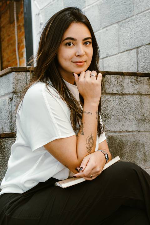nicole na parte de fora da cafeteria, próximo a escadaria, sentada, com o braço apoiado em livro em seu colo'