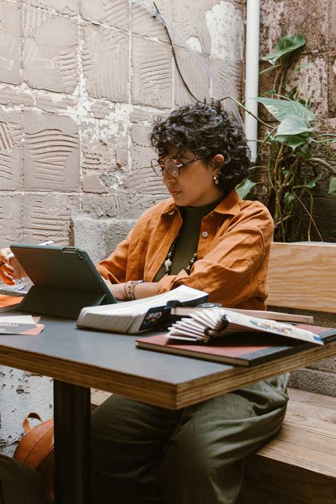 leticia sentada dentro da cafeteria, com o tablet, braços apoiados sobre a mesa'