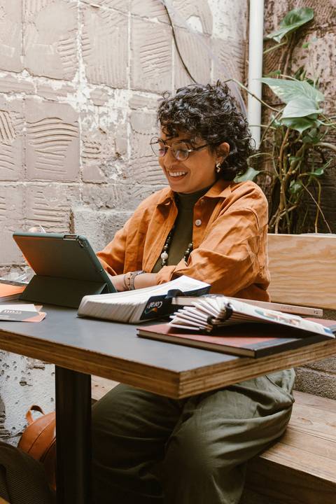 leticia sentada dentro da cafeteria, com o tablet, sorrindo enquanto mexe no tablet'