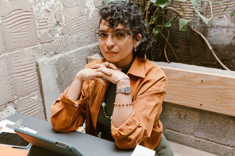 leticia sentada dentro da cafeteria, com o tablet, mãos cruzadas em frente ao rosto, novo ângulo e enquadramento'