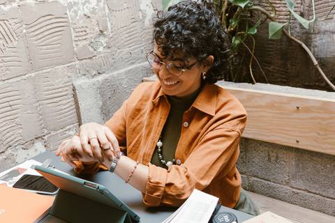 leticia sentada dentro da cafeteria, com o tablet,  enquanto mexe em seu próprio punho, sorrindo'